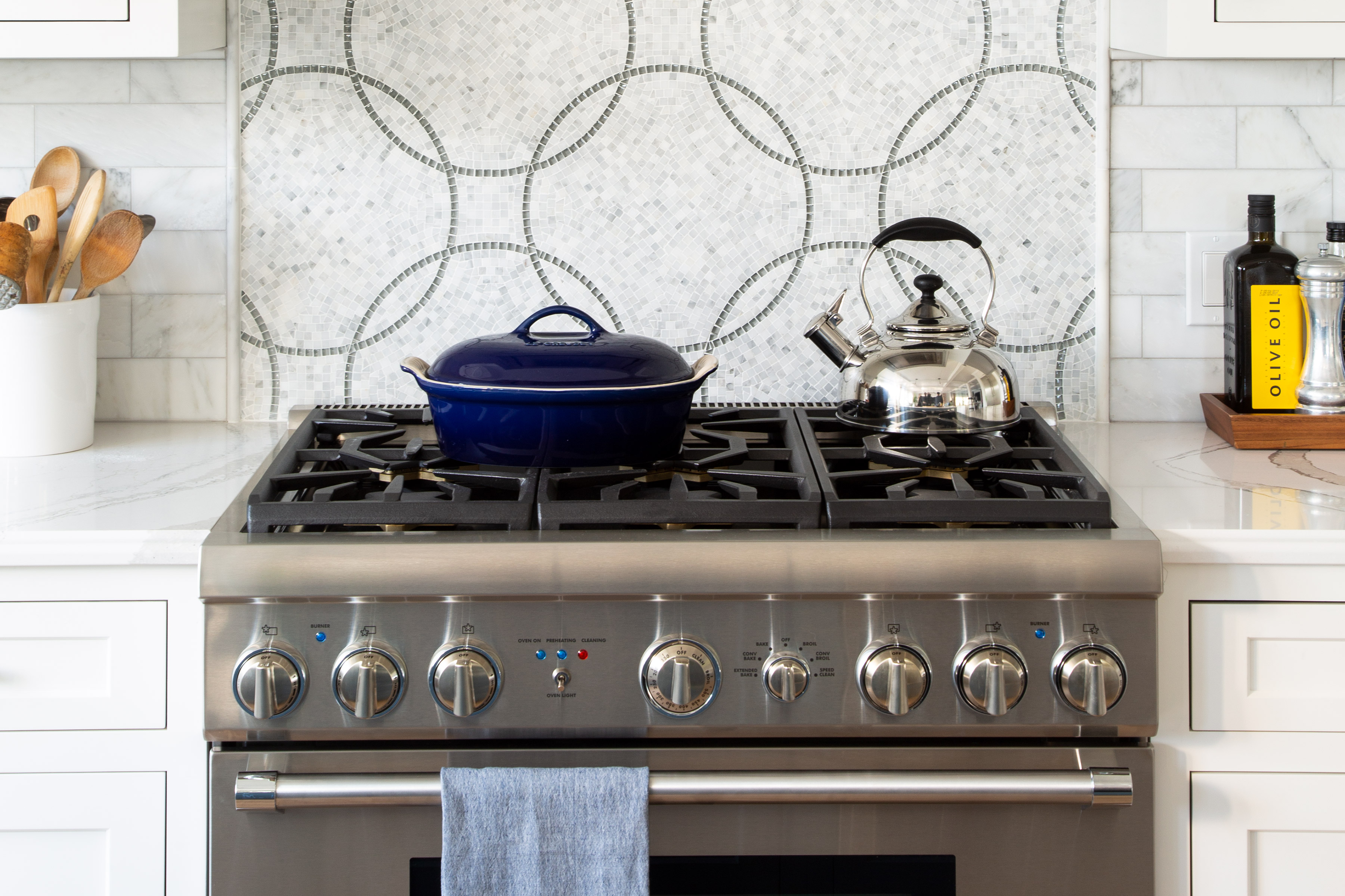A clean stainless steel gas stove with white cabinets.